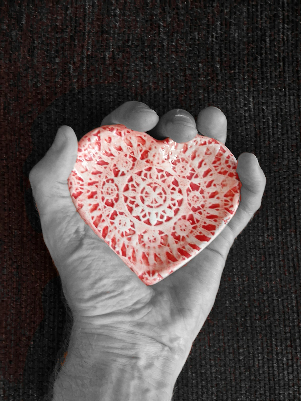 black and white picture of a hand holding a red decorated ceramic heart dish.  The heart is still coloured red