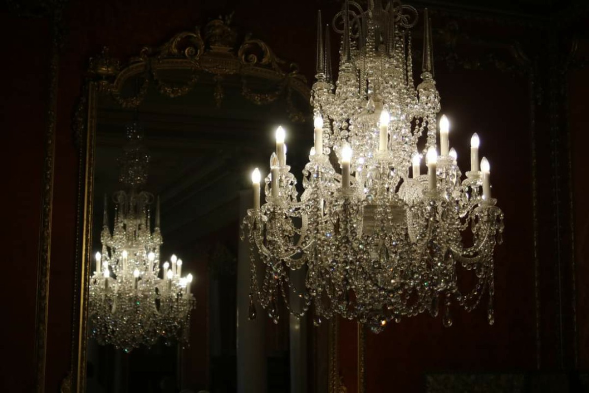 A crystal chandelier glows in the dark, reflected in a mirro in the background 