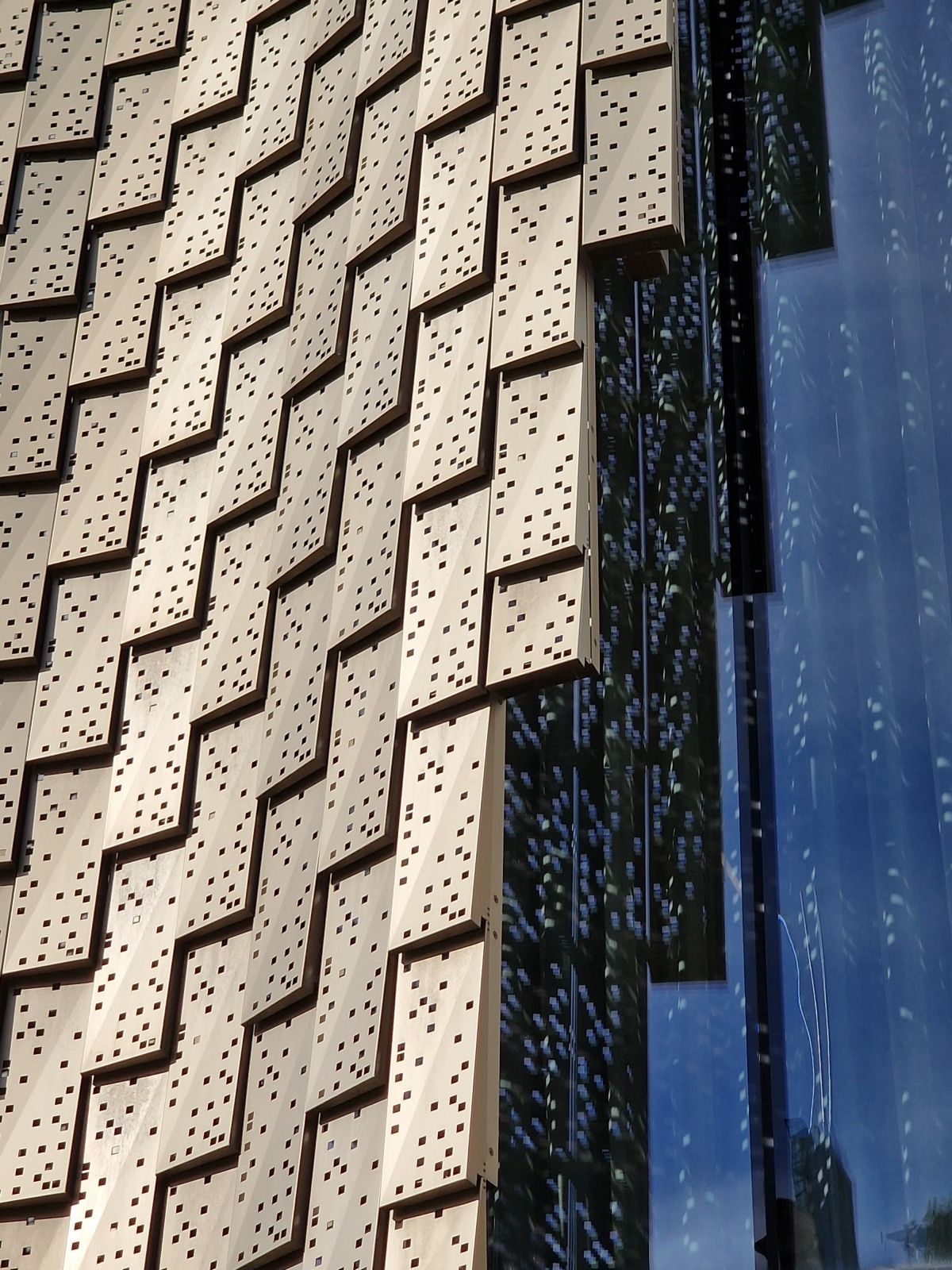 Close up of gold cladding tiles, creating a zig zag shape, and pierced with square holes.