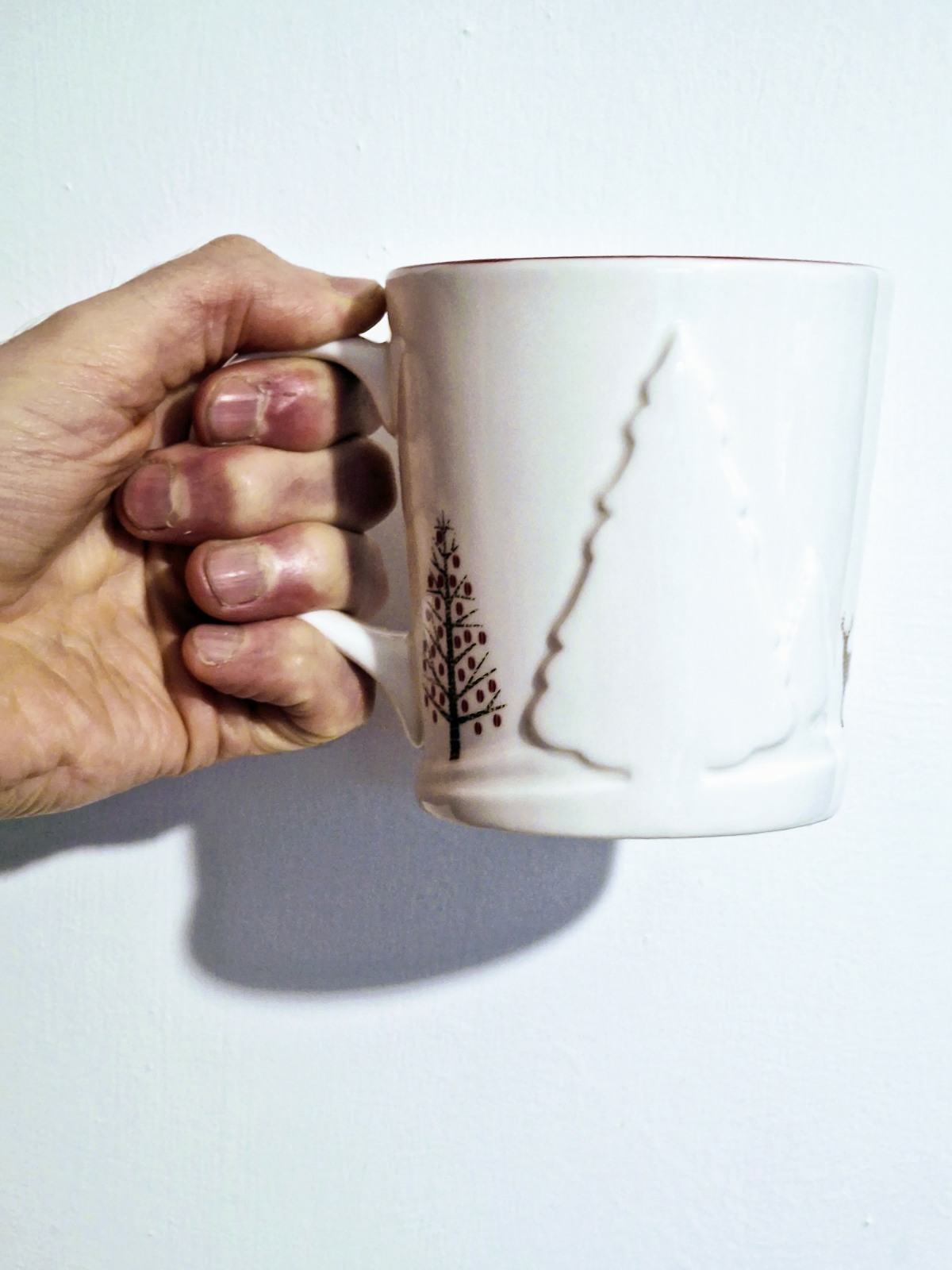 A hand holding a mug, which has an embossed christmas tree on it.