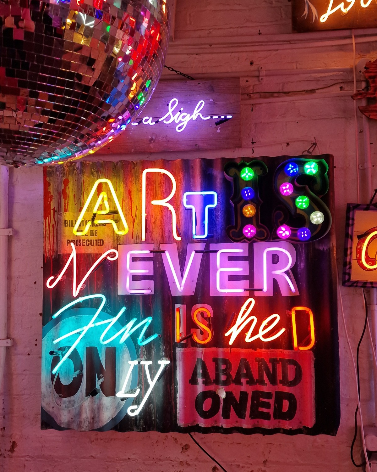 Neon letters and bulbs spell out "Art is never finished only abandoned"